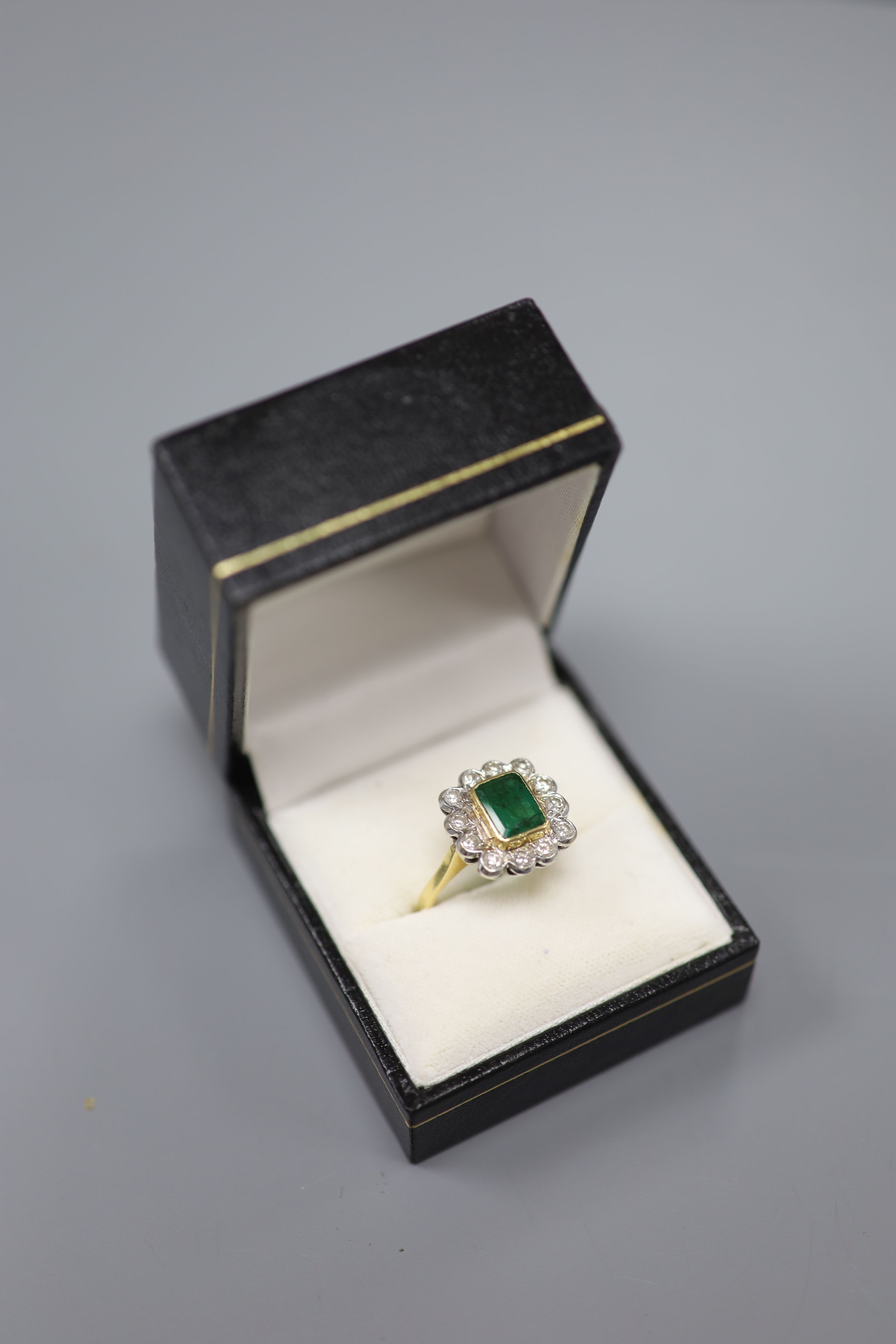 An emerald and diamond cluster ring, white and yellow metal setting (tests as 18ct), size Q, gross 6g.